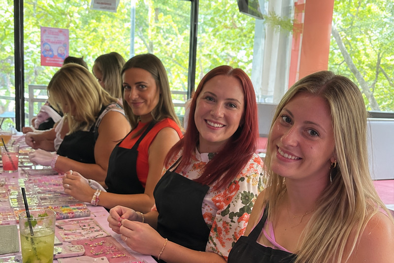 Friends in aprons at a long table of beads and gold charms