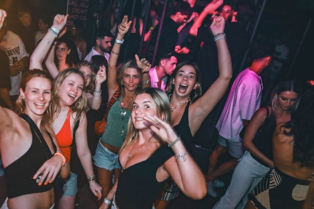 Friends dancing with their arms up and big smiles on a packed dance floor