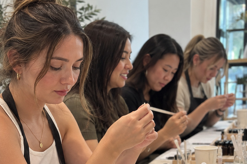 Hens in aprons smelling scent strips along a long table at a perfume making class