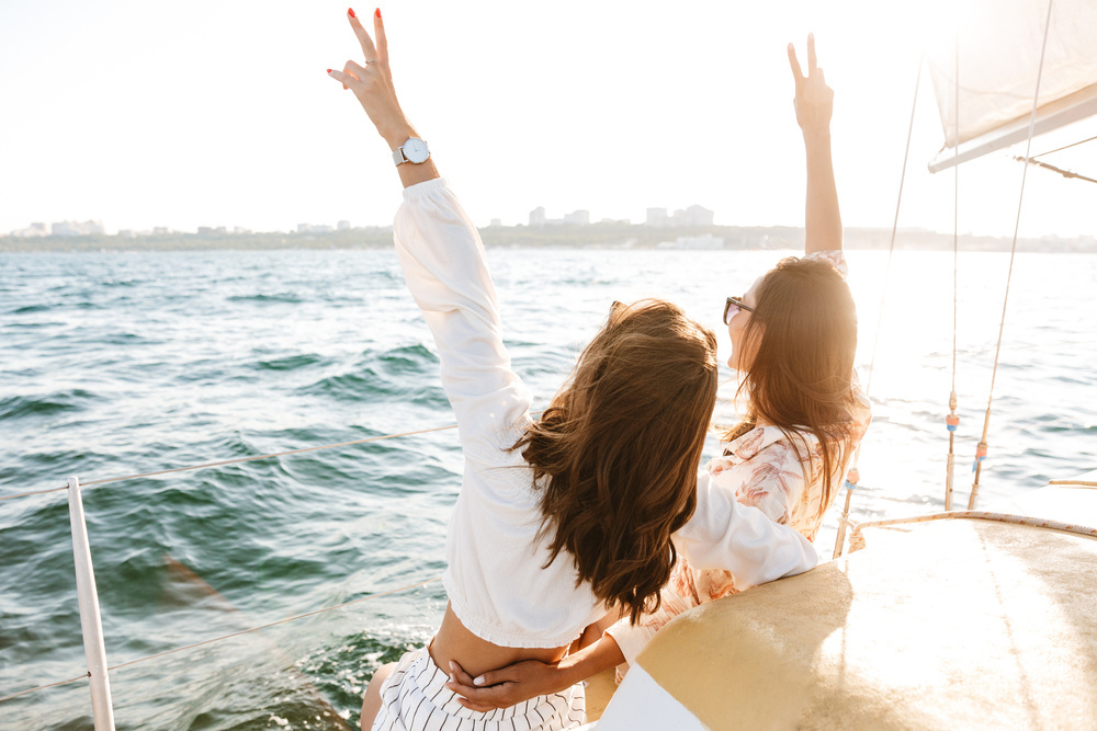 Two friends with their arms in the air on the deck of a boat, the city across the water