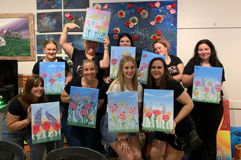 A group of friends holding up their finished floral paintings in an art studio