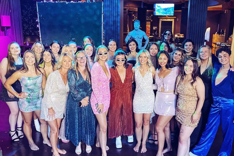 A big hens group in sequins at a male revue show with a performer behind