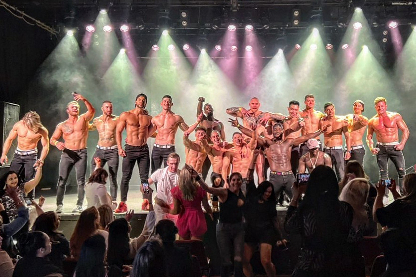 Male revue performers on a lit stage in front of a cheering crowd of hens