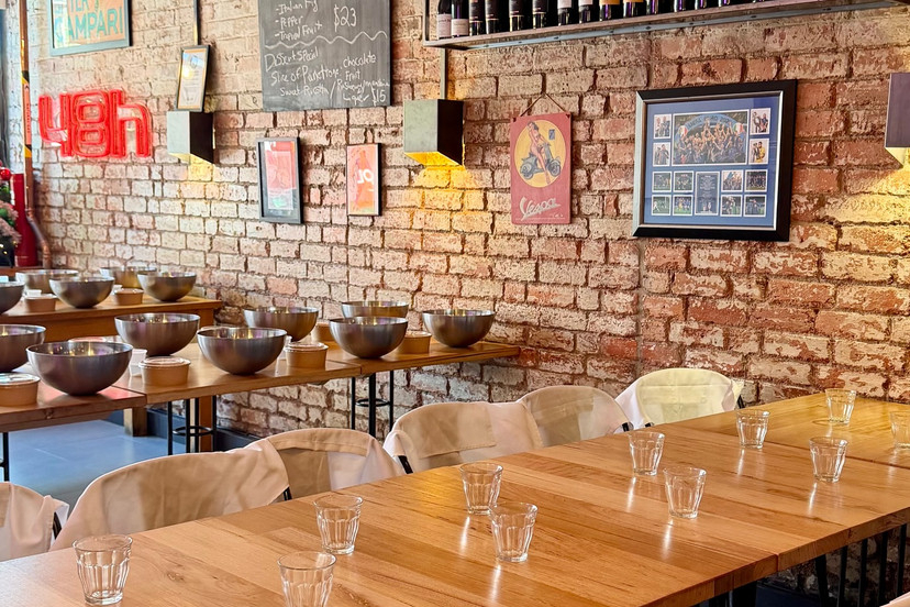 A brick walled Italian class room with mixing bowls set out on long timber tables and wine on the shelves