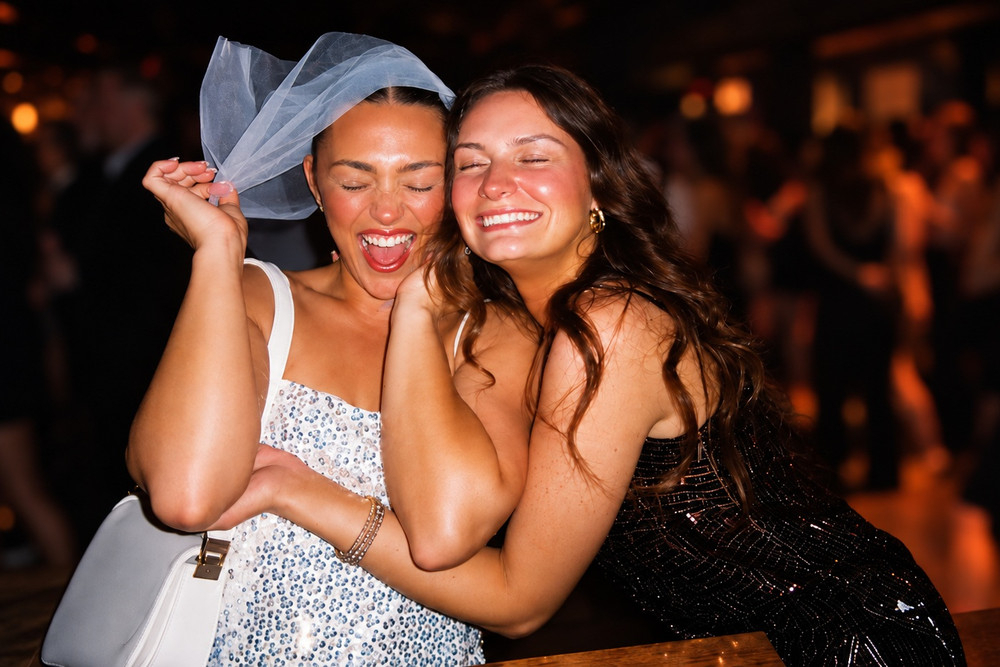 A bride to be in a short veil hugging a laughing friend later that night