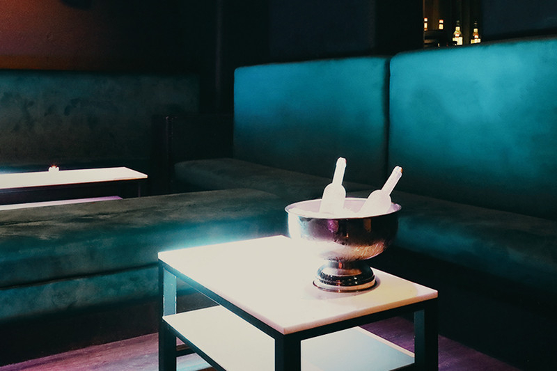 A dark velvet booth with a bottle of bubbly on ice on a low table