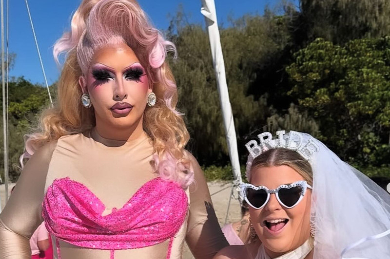 A drag queen in pink sequins beside the bride in a veil and heart sunglasses