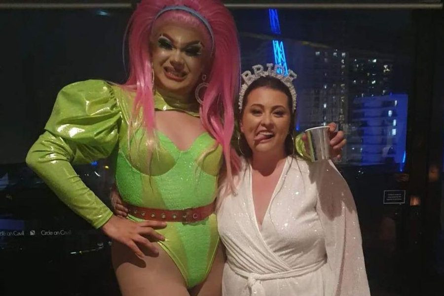 A drag queen in lime green with pink hair posing with the bride to be