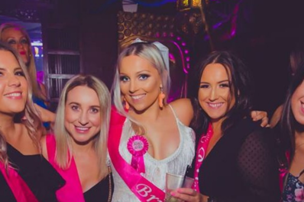 The bride in a pink sash with her friends in a lounge