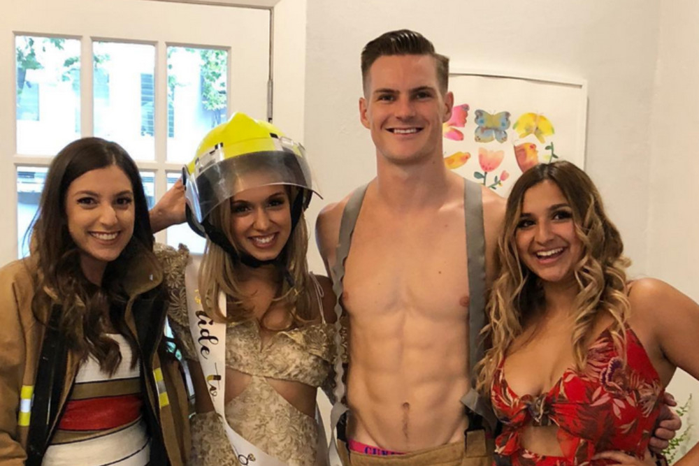 A shirtless fireman host with the bride wearing his helmet and her friends