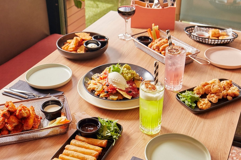 Share plates of spring rolls, wings and salads on a table by a window