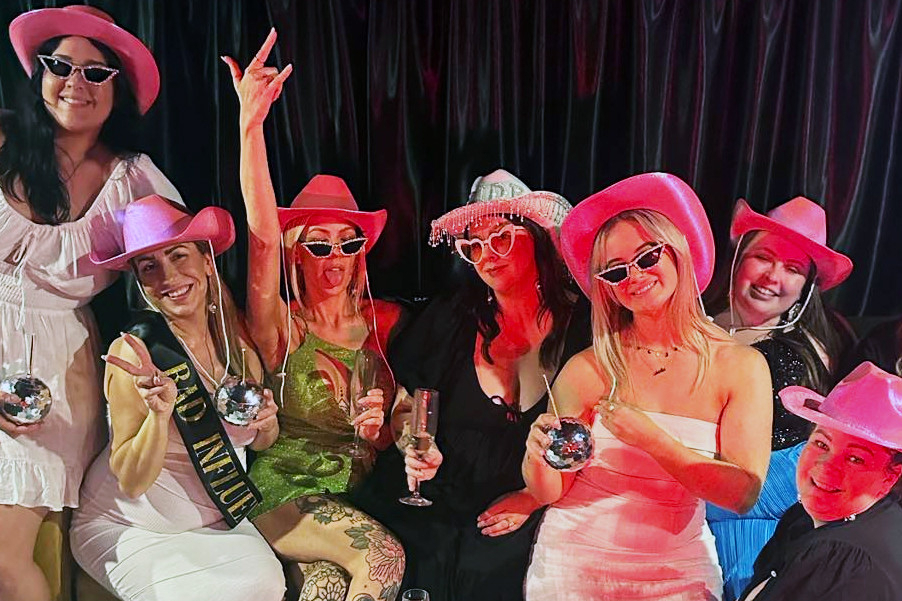 A cowgirl hens group in pink hats and heart sunglasses raising disco ball cups