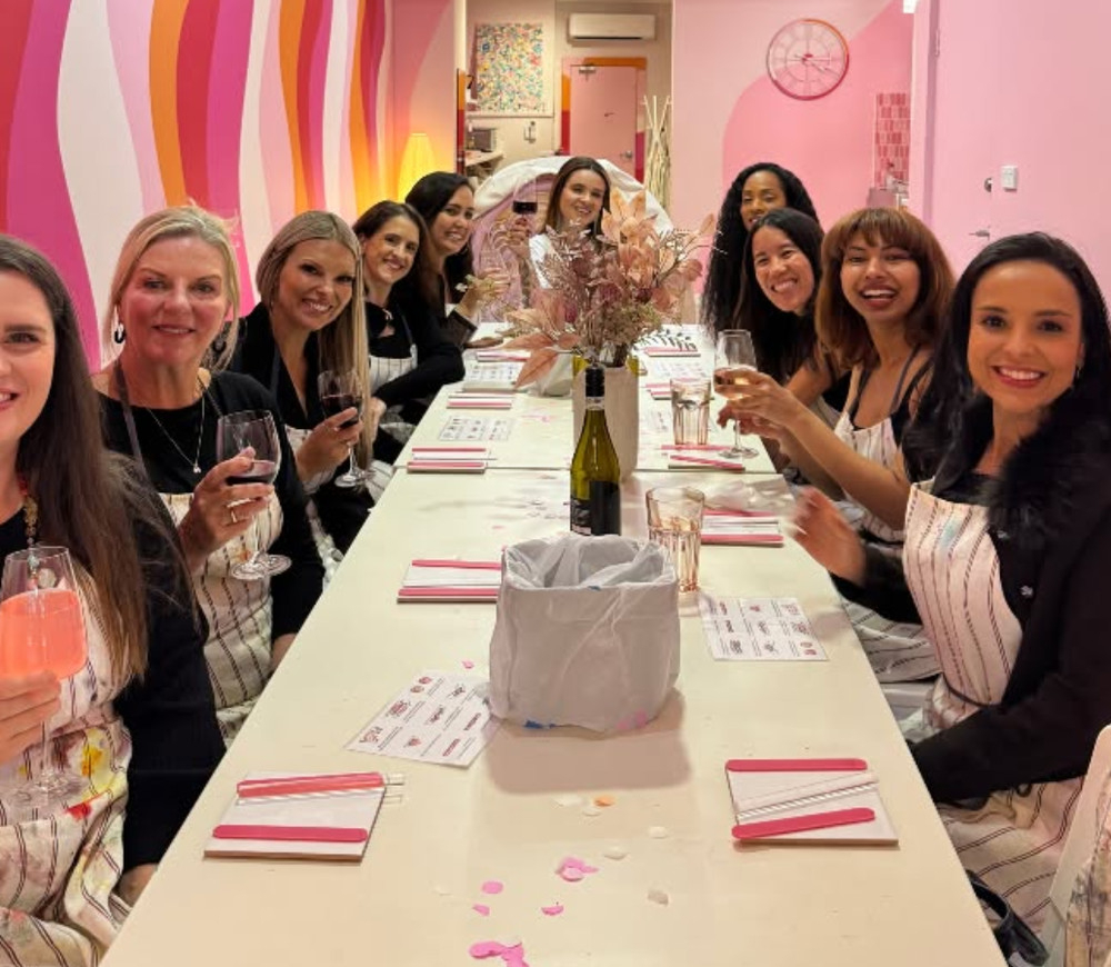 A long table of hens smiling with their glasses of bubbly raised