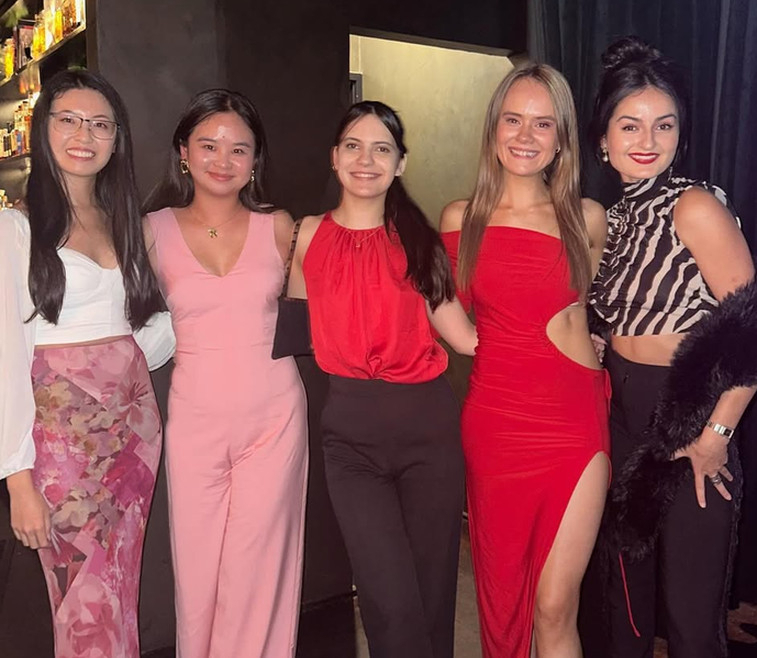 Five friends dressed up for a night out, smiling together inside a moody cocktail bar