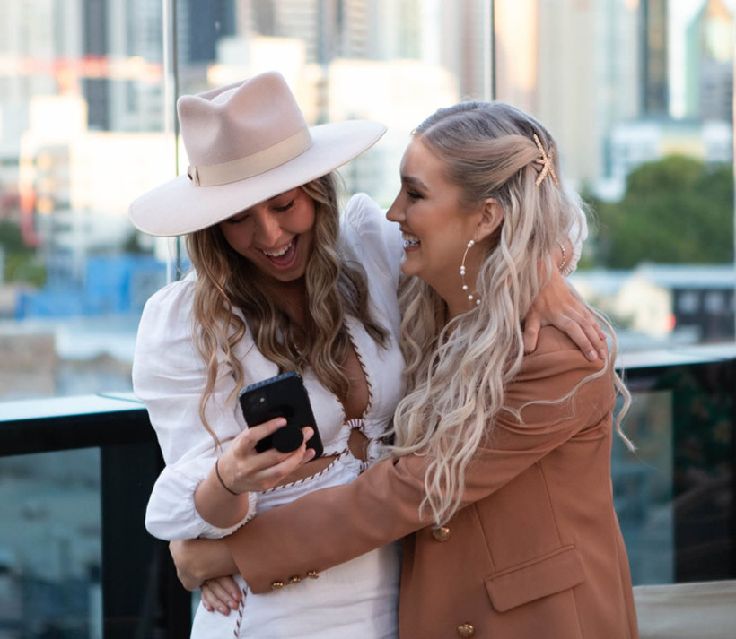 The bride in a white dress and hat hugging her friend on a city rooftop