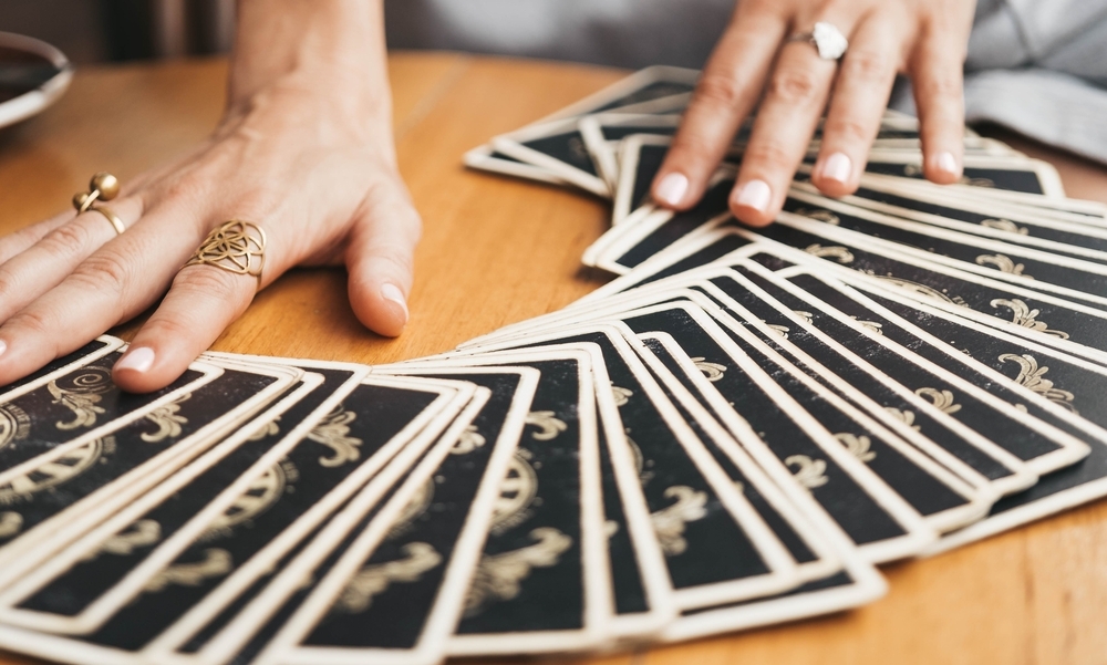 Hands with gold rings spreading tarot cards across a wooden table