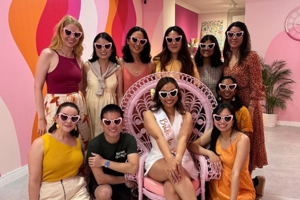 Bride to be in a pink peacock chair with her friends in heart sunglasses at the studio