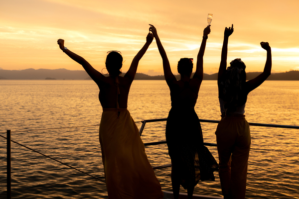 Four friends with their arms up on the water at sunset