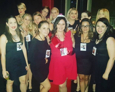 Kasey's hens group in black dresses and name badges at a night out, the bride in red with a sparkly tiara in the middle